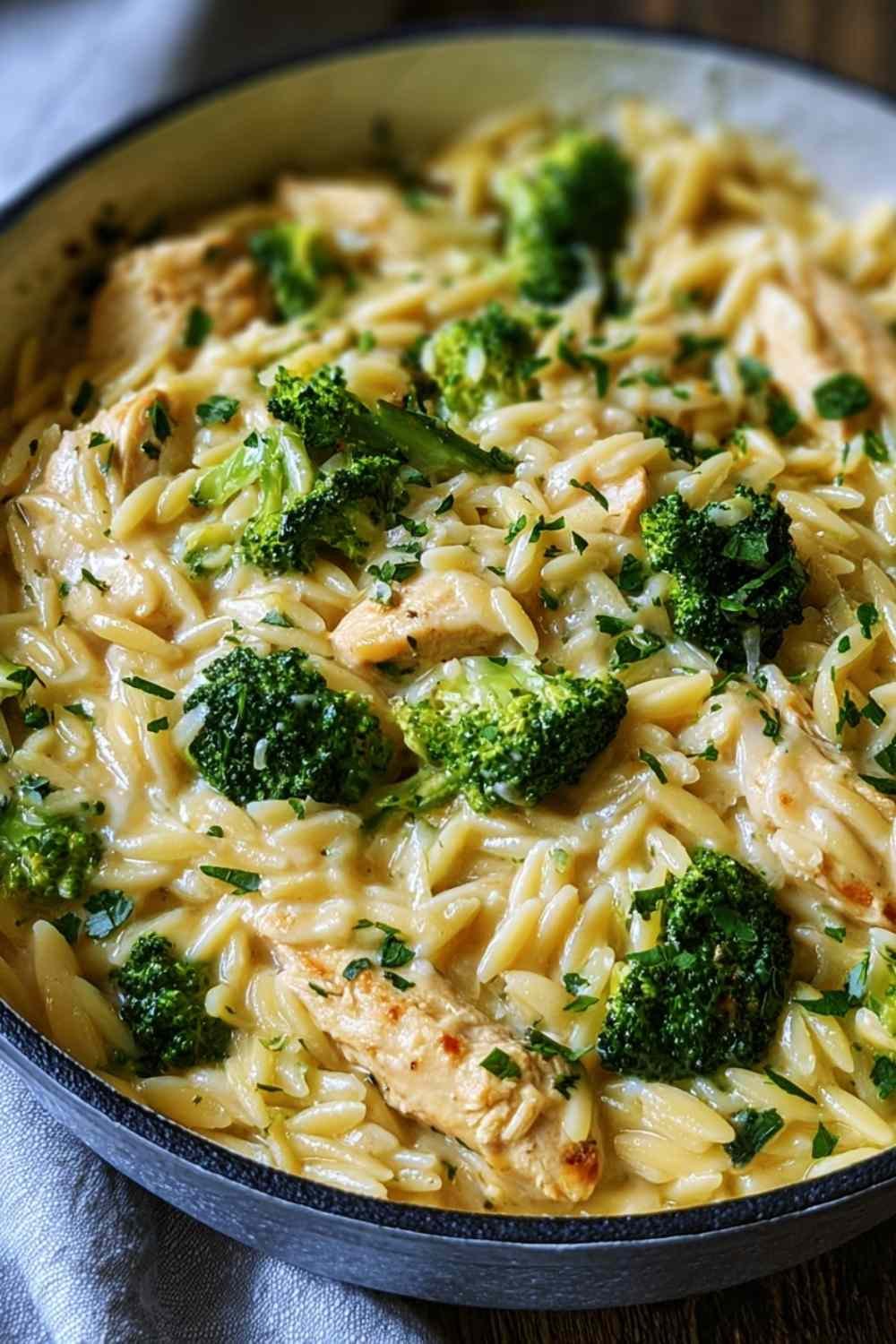Cheesy chicken broccoli orzo pasta in large skillet with melted cheddar cheese