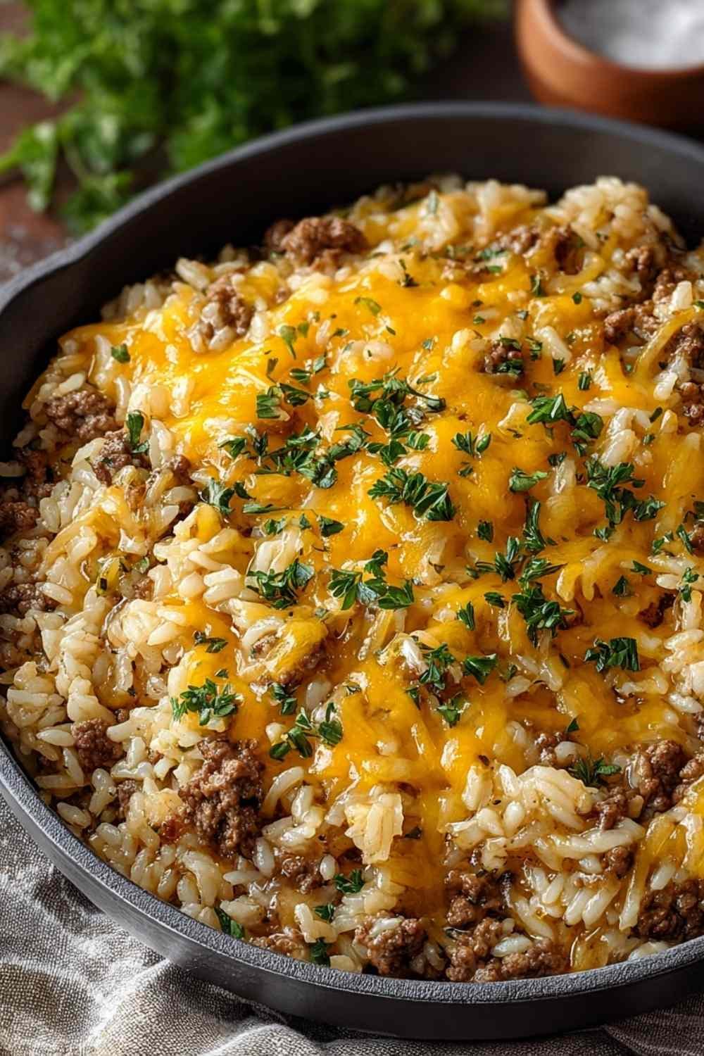 Cheesy hamburger rice casserole with melted cheddar cheese in a white baking dish garnished with fresh parsley