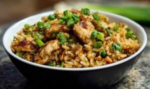 High protein crispy garlic chicken fried rice served in a white bowl with chopsticks and green onions