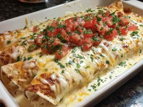 Queso chicken enchiladas in baking dish covered with melted cheese sauce