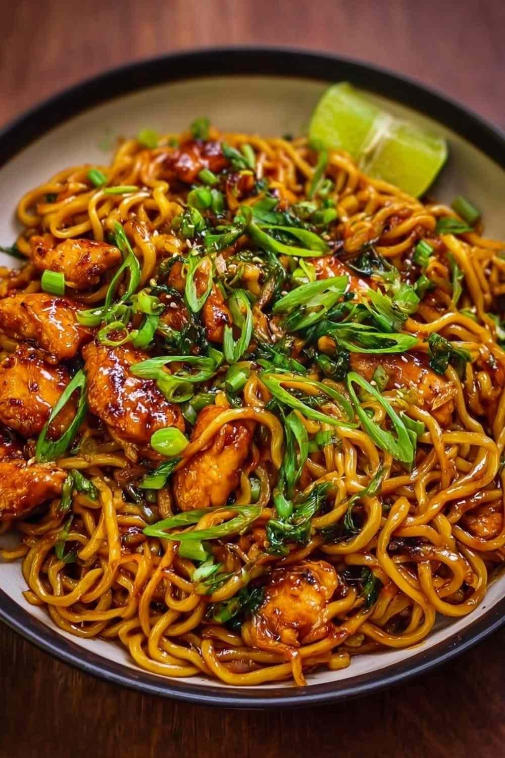 Sticky garlic chicken noodles in a white bowl garnished with green onions and sesame seeds