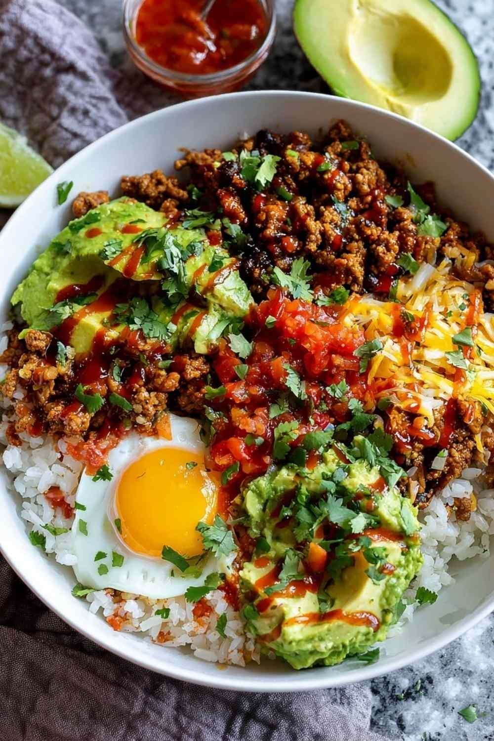 Taco rice bowl with seasoned beef, black beans, corn, tomatoes, lettuce, and cheese in white bowl