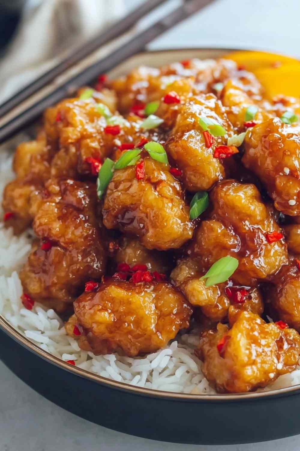 Hot orange chicken served over white rice garnished with green onions and sesame seeds