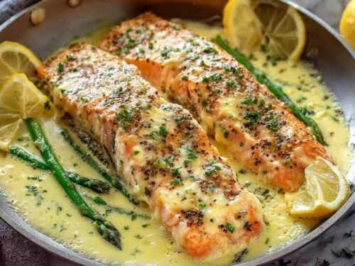Baked salmon with lemon butter cream sauce plated with fresh parsley and lemon slices