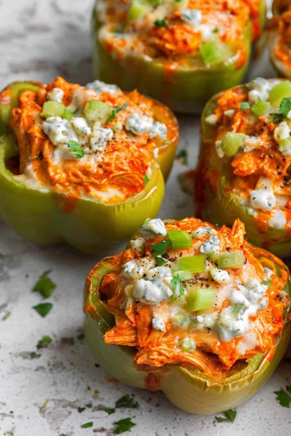 Buffalo chicken stuffed peppers on white plate drizzled with ranch dressing and fresh herbs