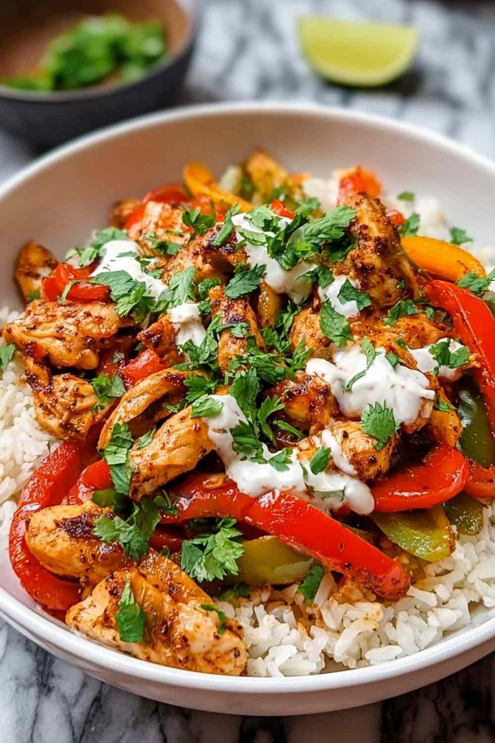 Chicken fajita rice bowl topped with sour cream, avocado, cheese, and cilantro in white bowl