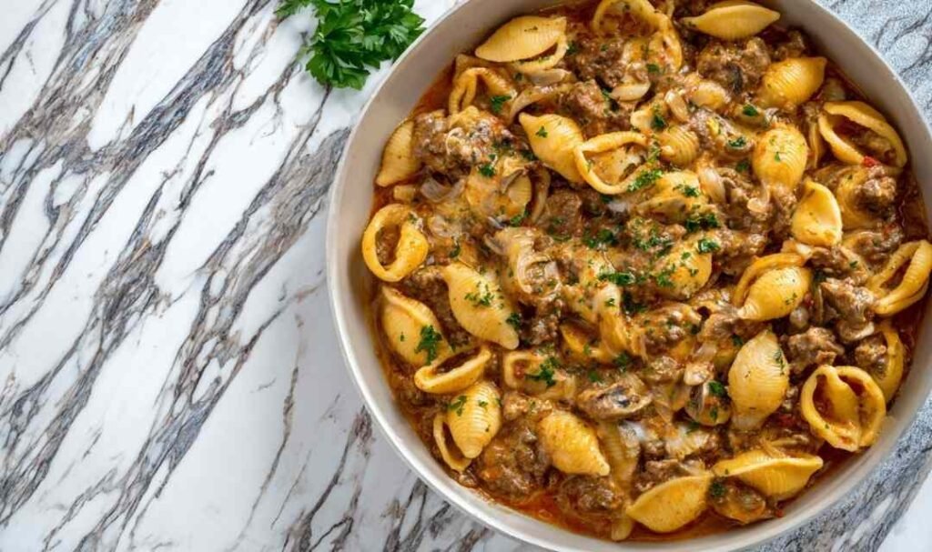 Creamy beef and shells pasta in large skillet with melted cheddar cheese and garnished with fresh parsley