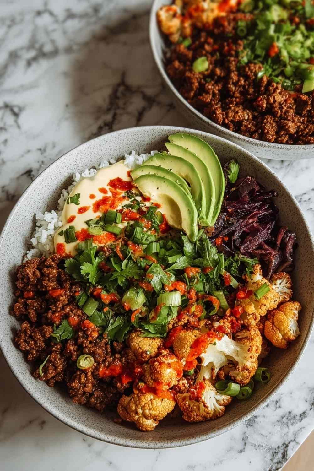 Crispy chile ground beef and cauliflower protein bowls topped with avocado cheese and cilantro in white serving bowl