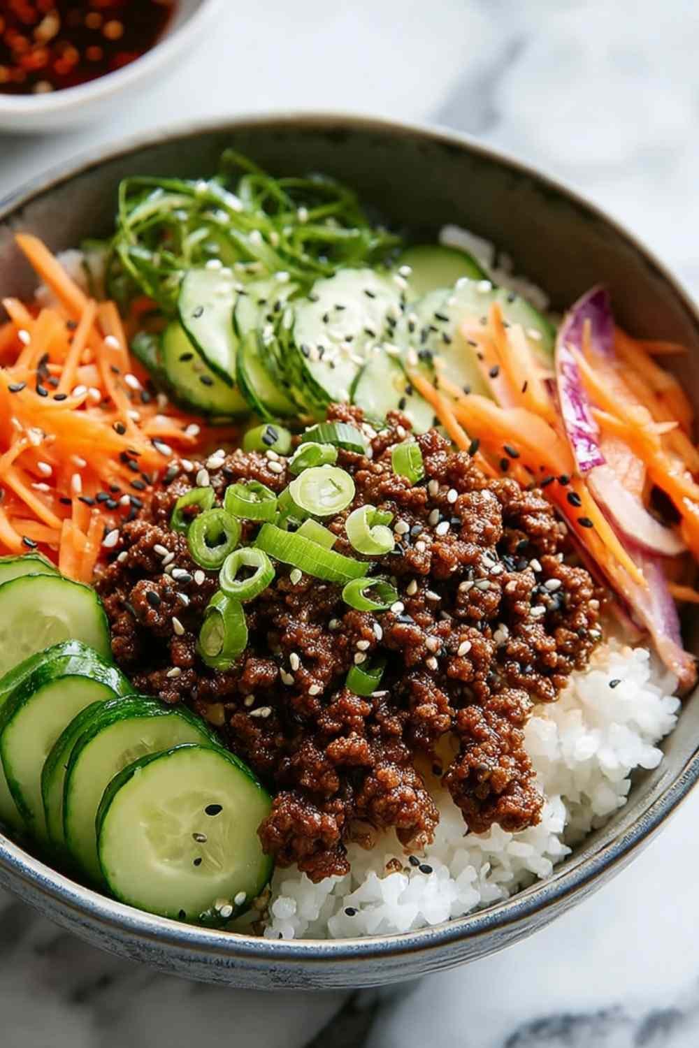 Korean ground beef bowl with rice, vegetables, and green onions garnish on white plate