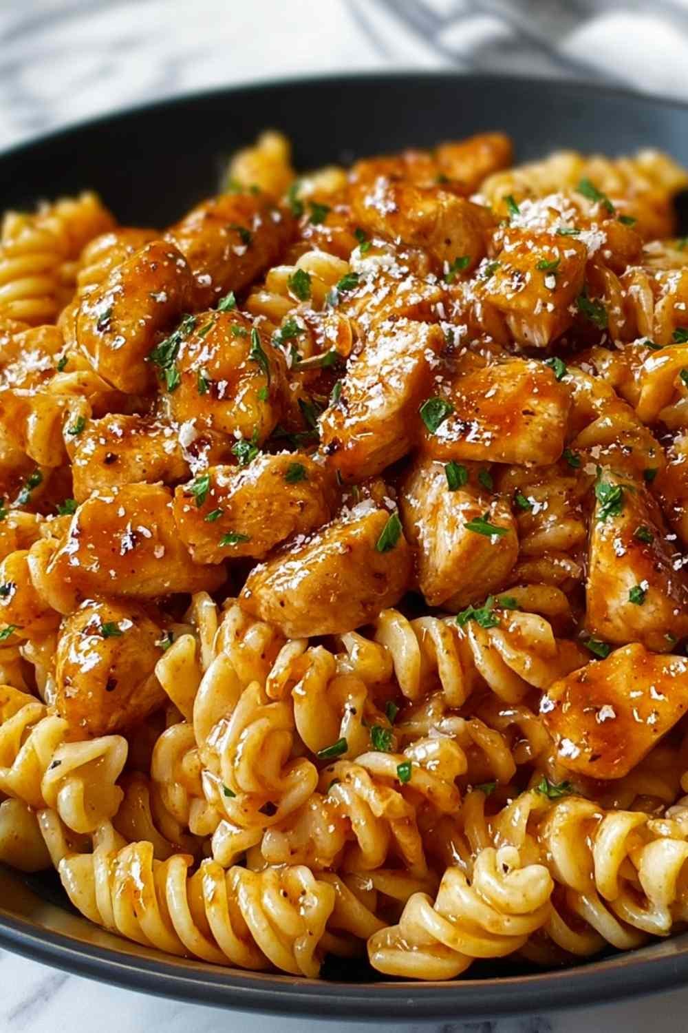 One-pot honey garlic BBQ chicken pasta with rotini spirals coated in sticky sweet sauce garnished with fresh parsley