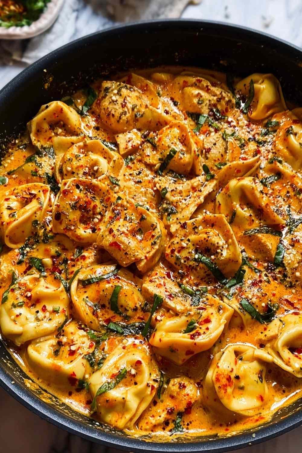 One-pot spicy garlic butter chicken tortellini with creamy sauce and fresh herbs in large pot