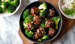 Sticky Mongolian meatballs and broccoli coated in glossy sauce in a skillet with sesame seeds