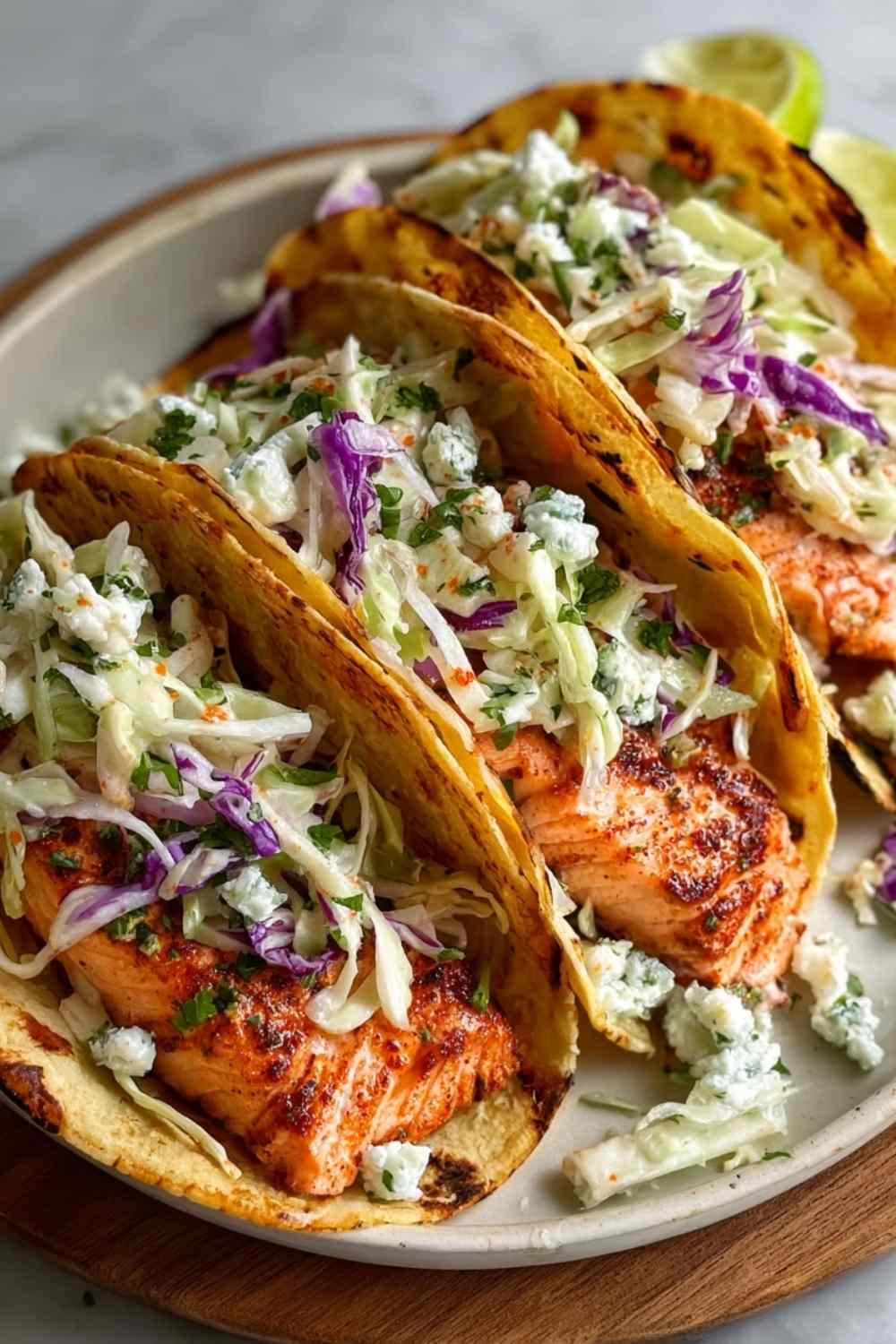 Air fryer salmon tacos topped with fresh cabbage slaw in warm corn tortillas on a white plate