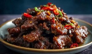 Crispy chilli beef with bell peppers and onions served over white rice on a dinner plate