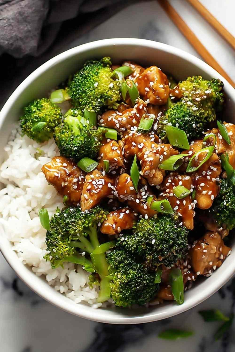 Skinny sesame chicken and broccoli stir-fry served over white rice with sesame seeds and green onions