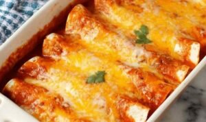 A baking dish of 5 ingredient beef enchiladas smothered in red enchilada sauce and melted Mexican cheese