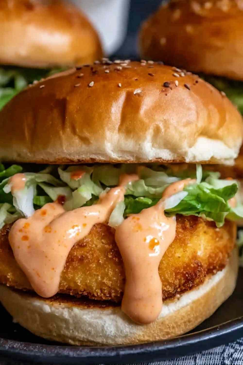 Crispy Bang Bang Chicken Sliders on a wooden board drizzled with creamy spicy Bang Bang sauce and topped with fresh lettuce