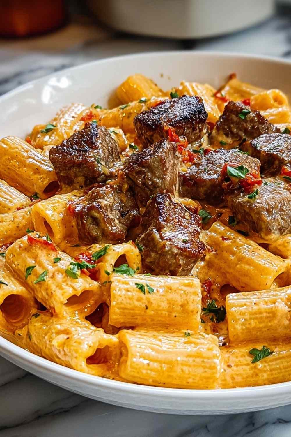 Cajun steak tips in cheesy rigatoni Parmesan sauce served in a skillet with fresh herbs