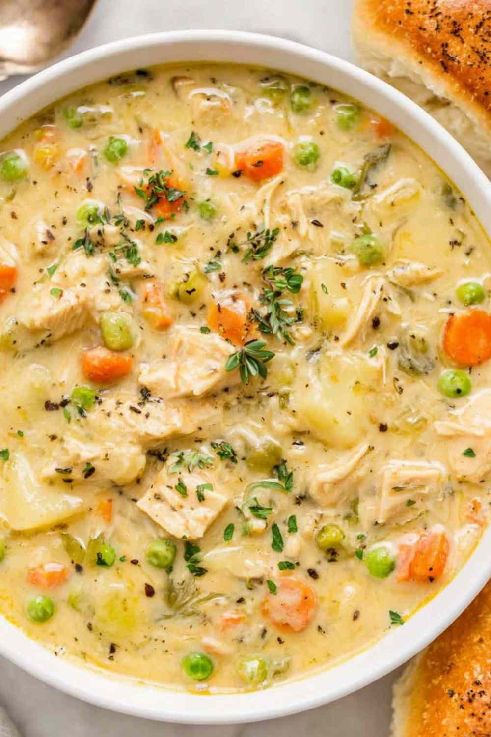 Creamy chicken pot pie soup served in a white bowl with fresh parsley garnish and warm buttered biscuits on the side, showing tender chicken pieces, carrots, and potatoes in a rich broth.