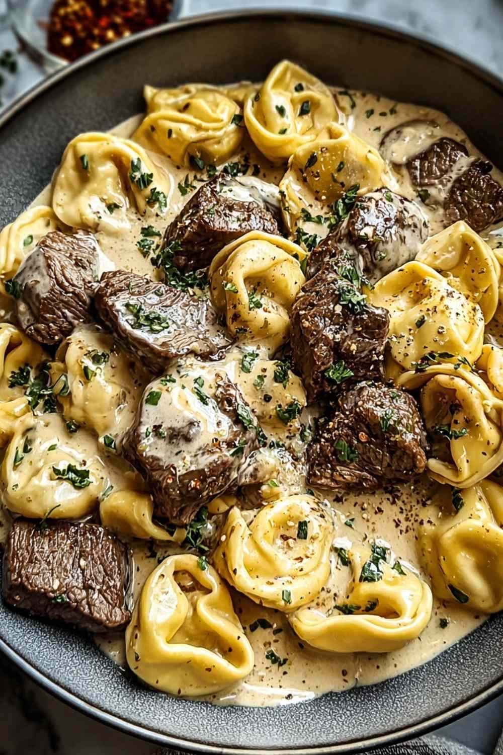 Cracked garlic steak tortellini in creamy sauce on white plate garnished with parsley