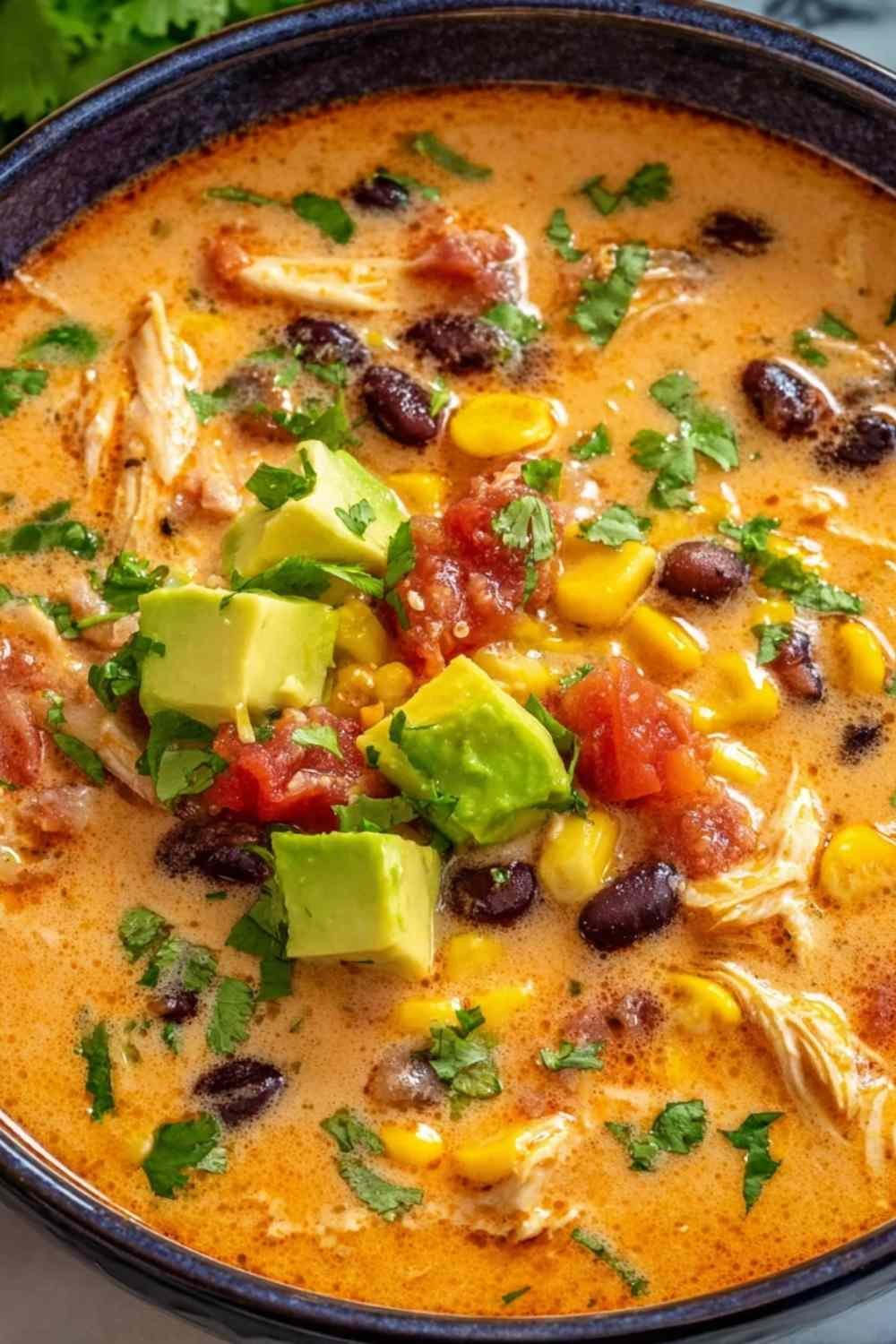 Creamy chicken enchilada soup in a white bowl with shredded chicken black beans kidney beans corn and shredded cheddar cheese in a rich smoky chili broth