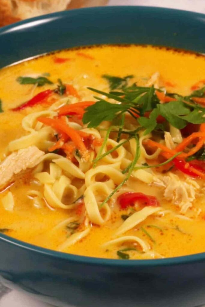 Overhead view of creamy chicken noodle soup with ramen noodles, golden coconut milk broth, and shredded chicken garnished with fresh cilantro