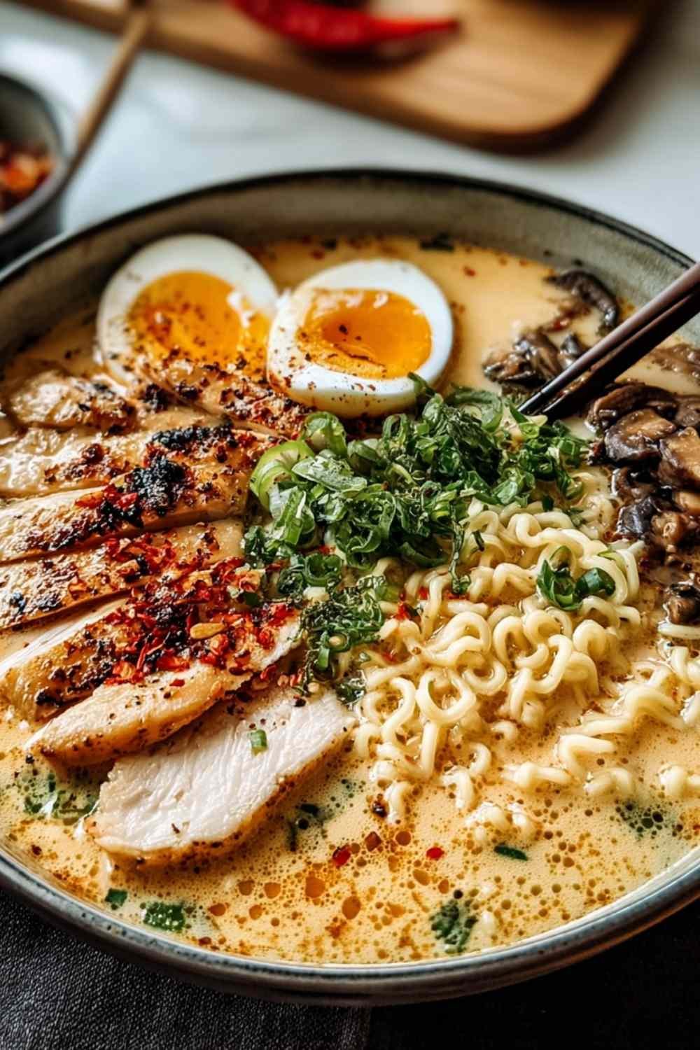 A bowl of creamy garlic chicken ramen topped with sliced chicken breast, green onions, and fresh cilantro
