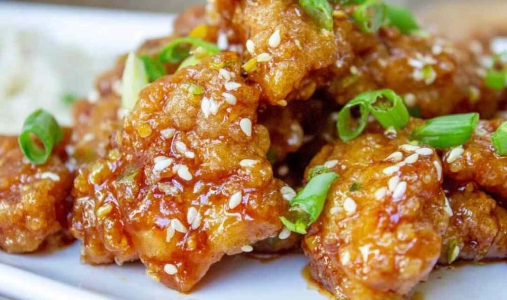 Crispy Chinese Honey Garlic Chicken on a white plate garnished with toasted sesame seeds and sliced green onions