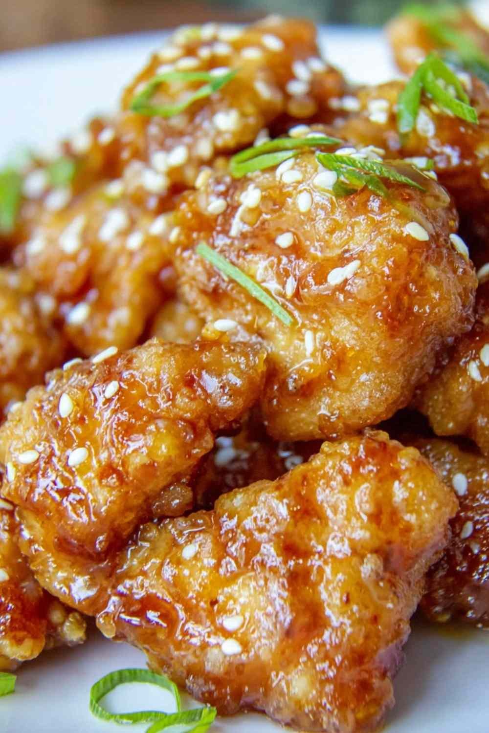 Crispy Chinese Honey Garlic Chicken on a white plate garnished with toasted sesame seeds and sliced green onions