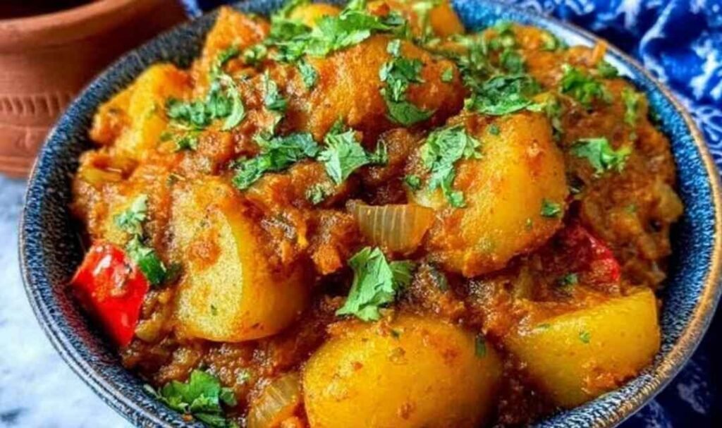 Overhead view of Persian Potato Curry Dopiazeh Aloo in a wide bowl with golden turmeric sauce, soft potato cubes, and fresh cilantro garnish alongside warm flatbread