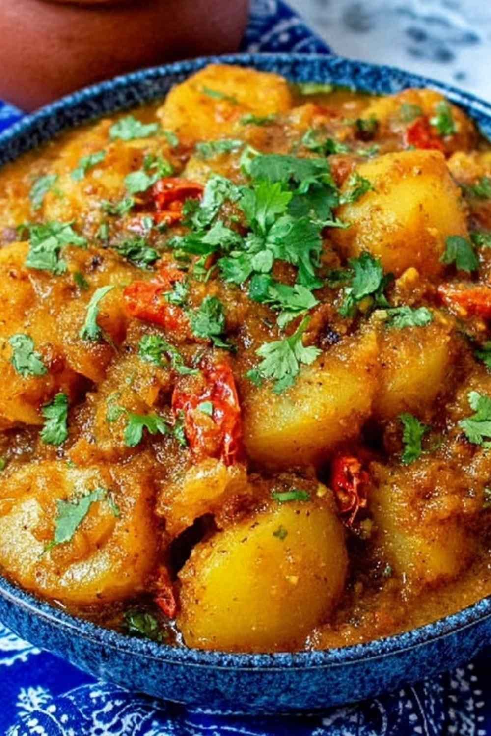 Overhead view of Persian Potato Curry Dopiazeh Aloo in a wide bowl with golden turmeric sauce, soft potato cubes, and fresh cilantro garnish alongside warm flatbread