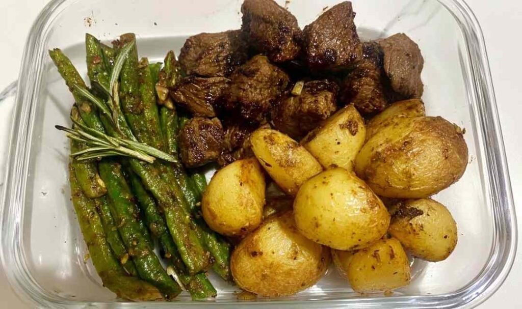 Overhead view of Garlic Balsamic Steak Bites in glossy balsamic garlic glaze served with crispy roasted baby potatoes and blistered green beans on a white plate