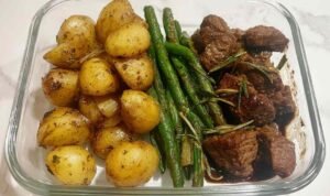 Overhead view of Garlic Balsamic Steak Bites in glossy balsamic garlic glaze served with crispy roasted baby potatoes and blistered green beans on a white plate