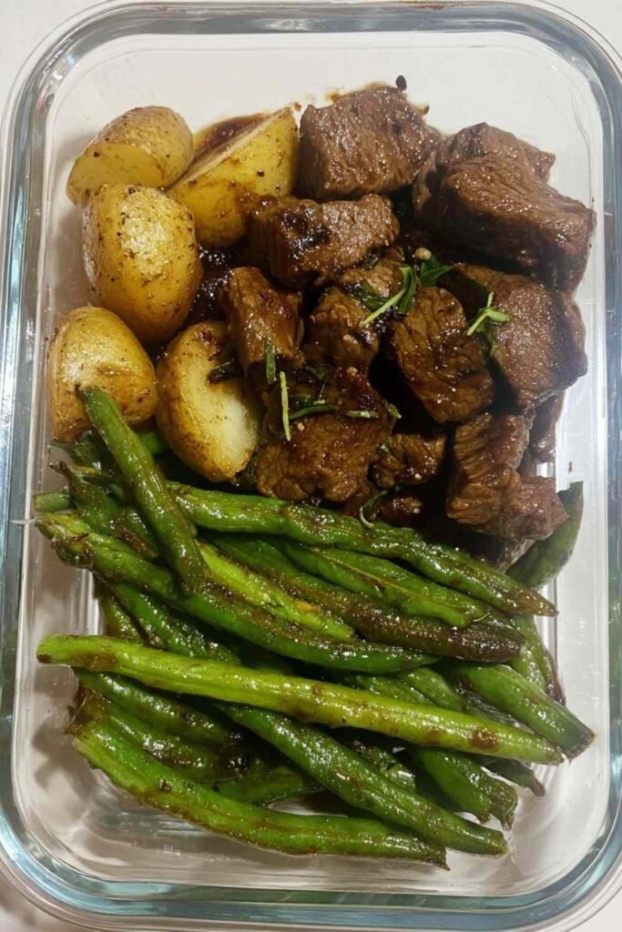 Overhead view of Garlic Balsamic Steak Bites in glossy balsamic garlic glaze served with crispy roasted baby potatoes and blistered green beans on a white plate
