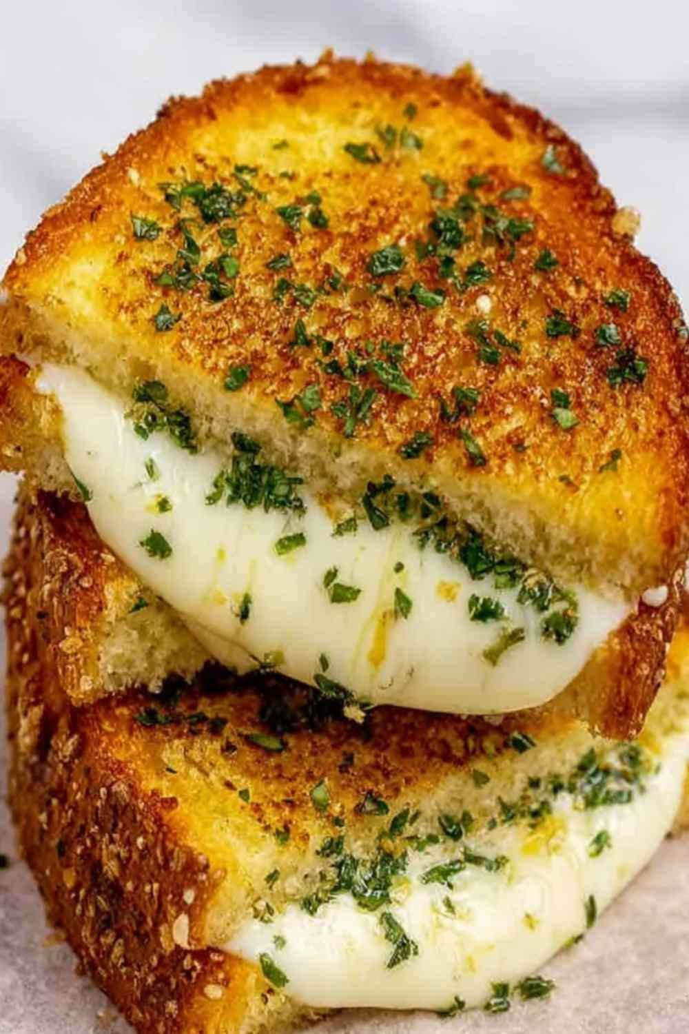 Garlic bread grilled cheese sandwich sliced diagonally showing a gooey mozzarella and cheddar cheese pull on a wooden board