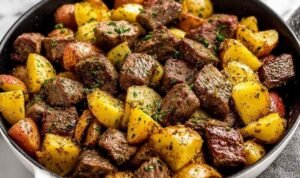 Garlic butter steak bites with baby potatoes and fresh herbs in a cast iron skillet ready to serve
