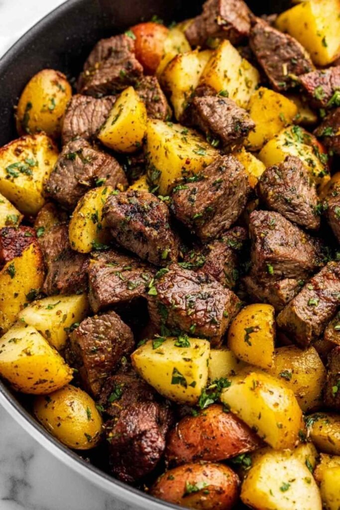 Garlic butter steak bites with baby potatoes and fresh herbs in a cast iron skillet ready to serve