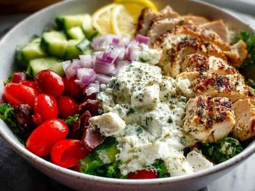 Greek chicken bowls with marinated chicken, fresh vegetables, rice, feta cheese, and tzatziki sauce