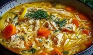 Bowl of Greek lemon chicken soup with orzo pasta, shredded chicken, vegetables, and fresh parsley garnish