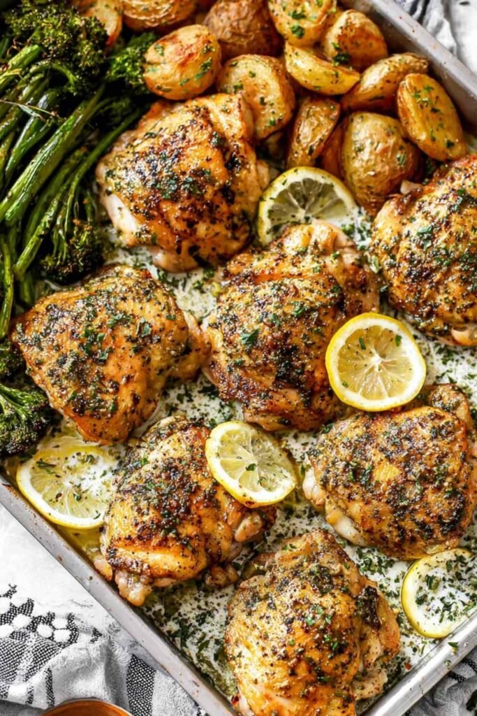 Juicy lemon garlic chicken thighs on a foil-lined sheet pan with roasted baby potatoes and broccoli