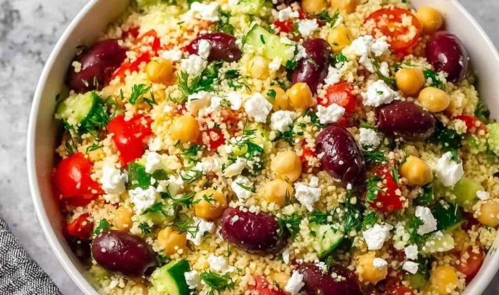 Light Mediterranean couscous salad in a white serving bowl with feta chickpeas Kalamata olives cucumber and fresh herbs