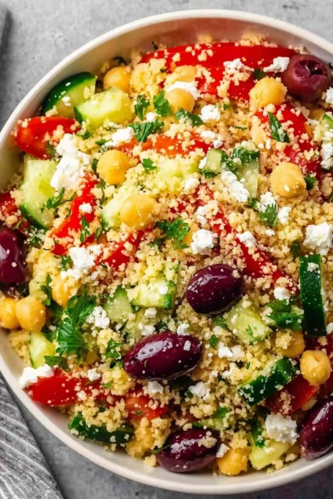 Light Mediterranean couscous salad in a white serving bowl with feta chickpeas Kalamata olives cucumber and fresh herbs