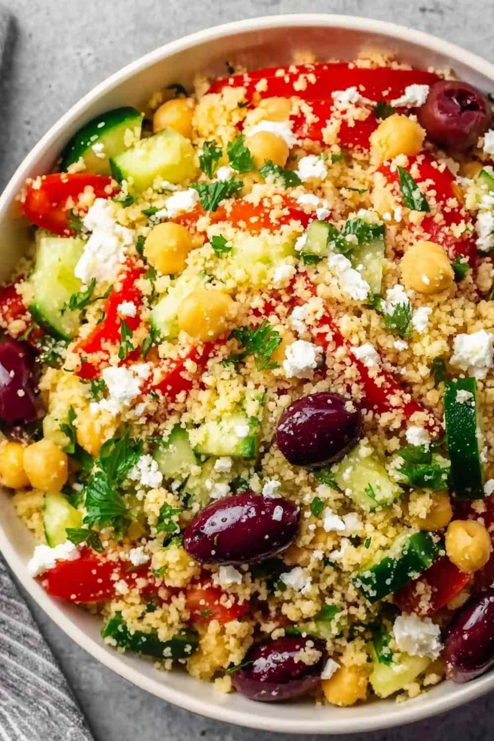 Light Mediterranean couscous salad in a white serving bowl with feta chickpeas Kalamata olives cucumber and fresh herbs