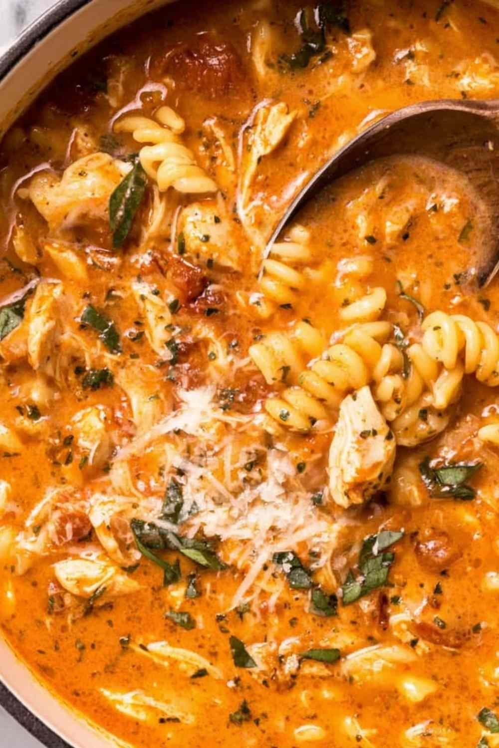 Creamy marry me chicken soup with rotini pasta, sun-dried tomatoes, and fresh basil garnished with parmesan cheese