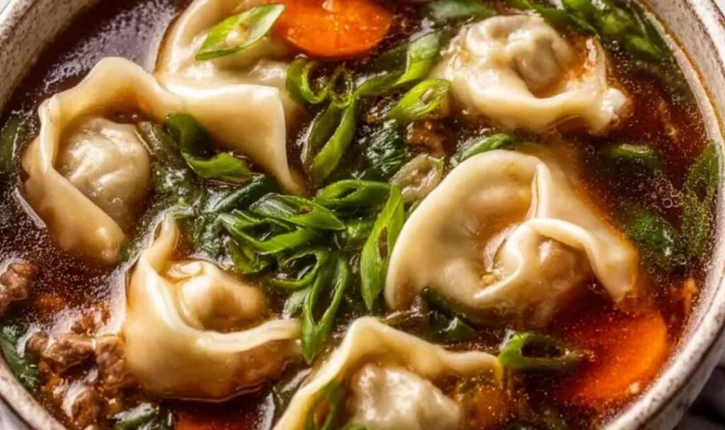 Potsticker soup in a white bowl with plump beef dumplings wilted spinach and chopped green onions in a clear golden ginger garlic chicken broth