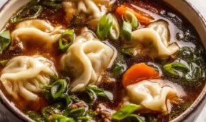 Potsticker soup in a white bowl with plump beef dumplings wilted spinach and chopped green onions in a clear golden ginger garlic chicken broth