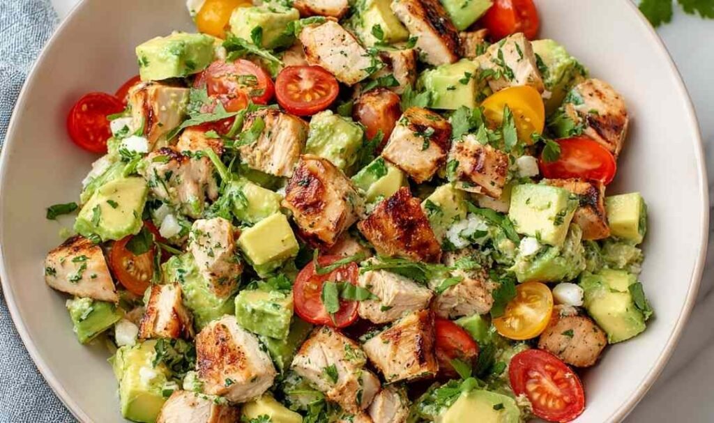 Avocado Chicken Salad Recipe in a large white bowl with cherry tomatoes, diced cucumber, fresh cilantro, and a lime wedge