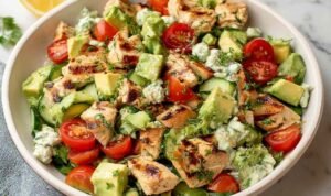 Avocado Chicken Salad Recipe in a large white bowl with cherry tomatoes, diced cucumber, fresh cilantro, and a lime wedge
