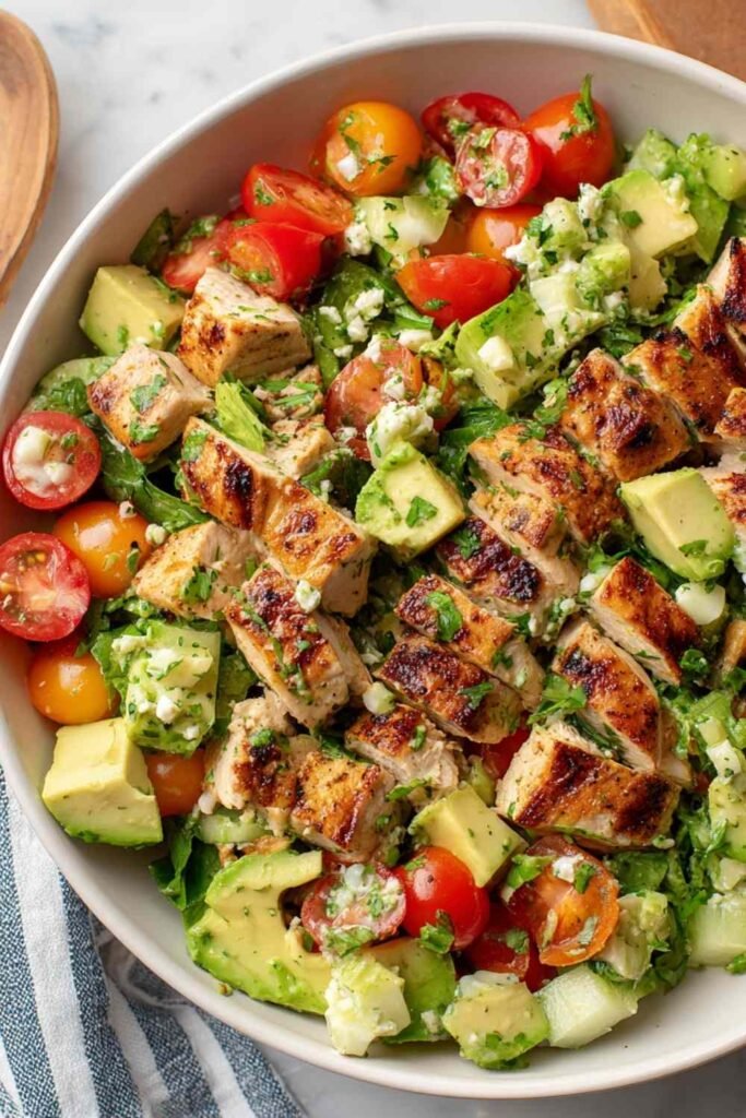 Avocado Chicken Salad Recipe in a large white bowl with cherry tomatoes, diced cucumber, fresh cilantro, and a lime wedge