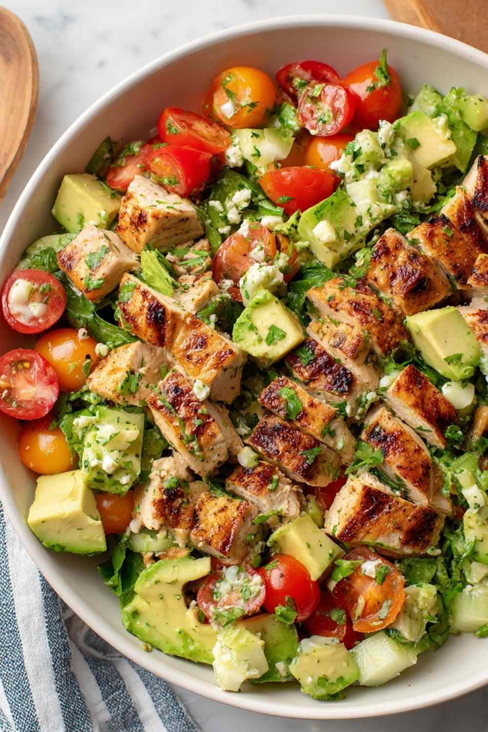 Avocado Chicken Salad Recipe in a large white bowl with cherry tomatoes, diced cucumber, fresh cilantro, and a lime wedge